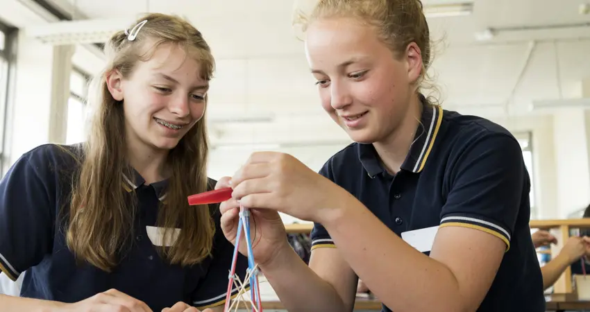 Two girls building a small tower shape project.