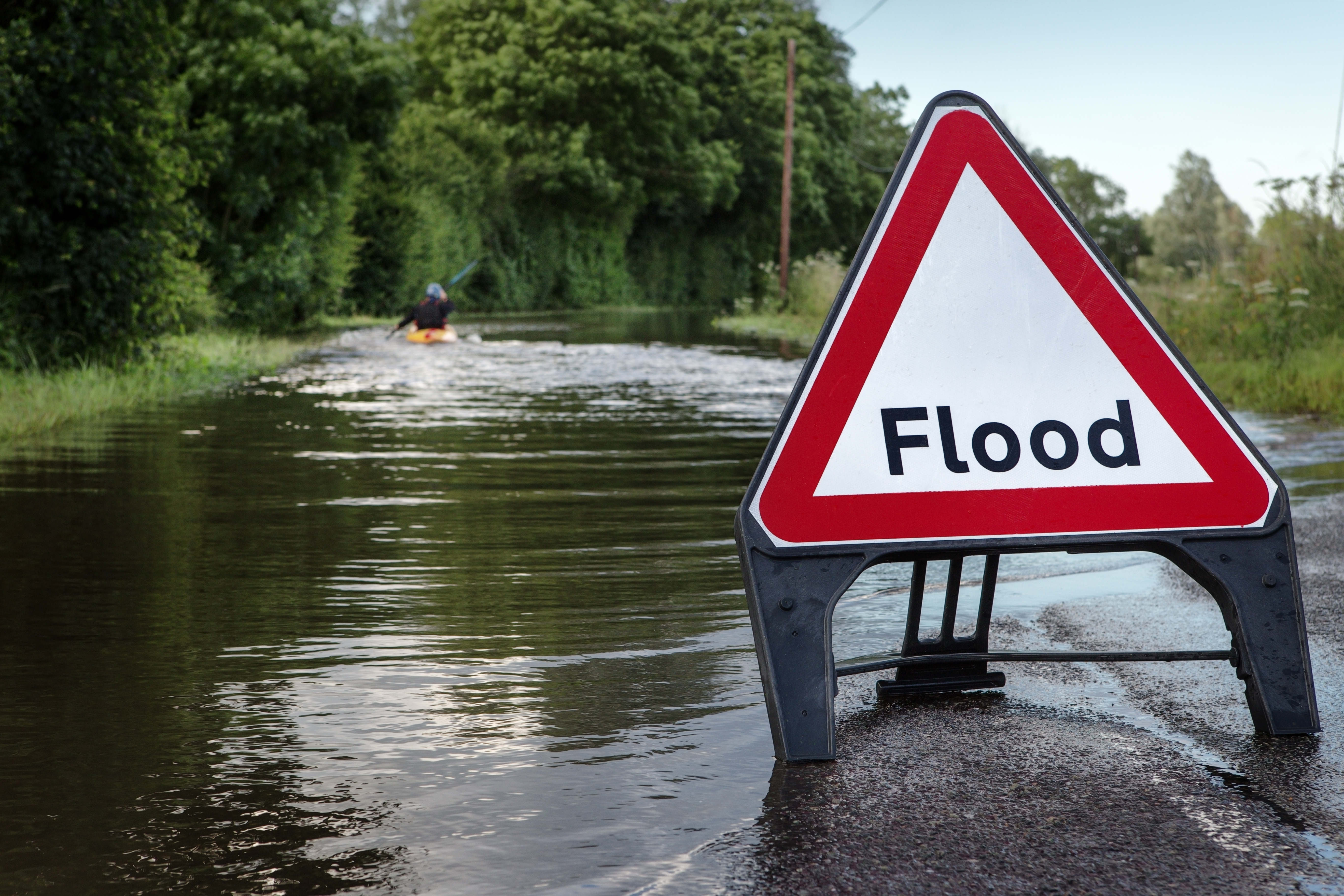 Triangle flood warning sign in foreground of flooded road