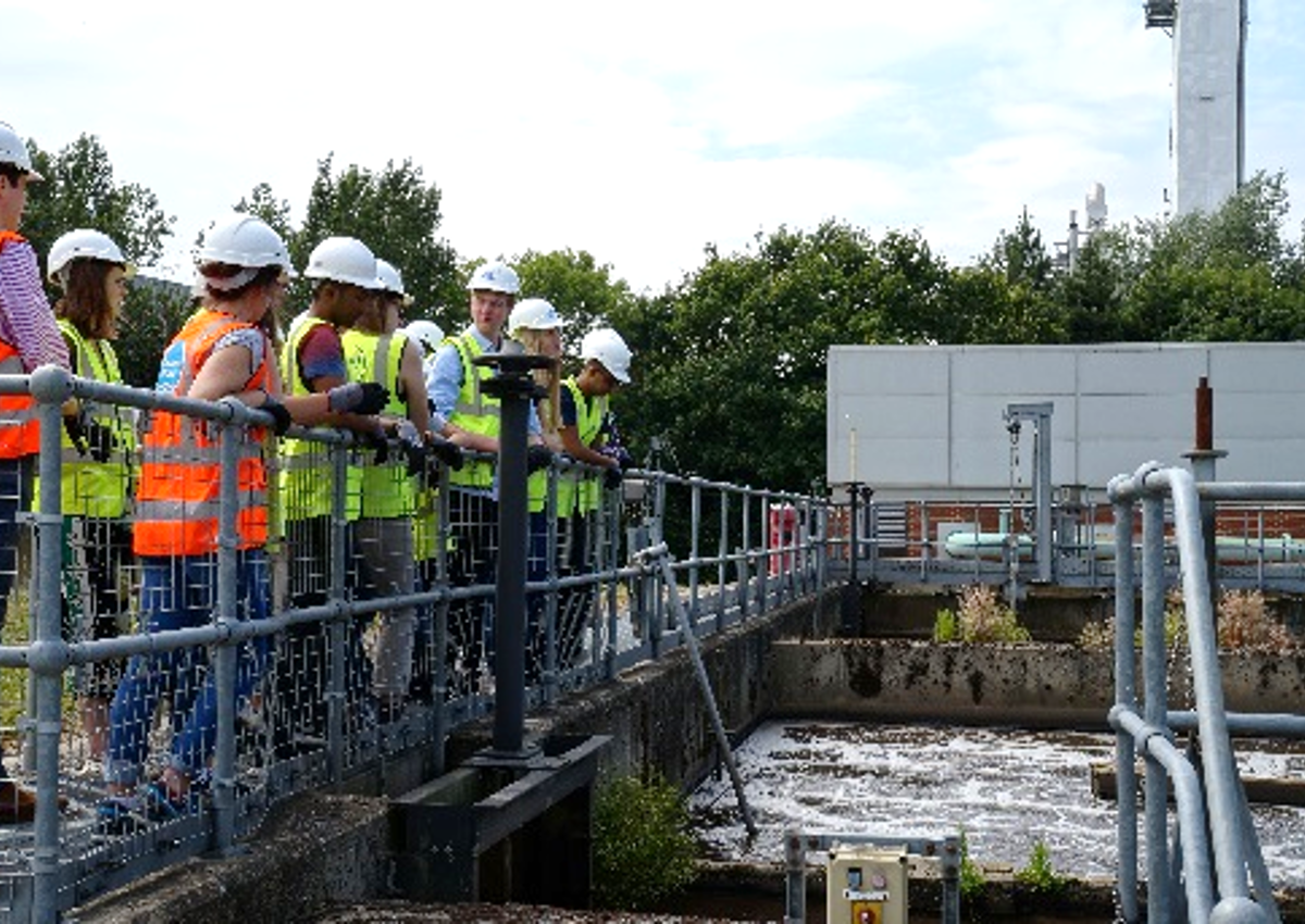 Group of people ona bridge wearing hard hats and high-visibility vests looking at water and pipes