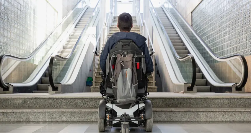 Man in wheelchair at bottom of inaccessible escalators, looking up
