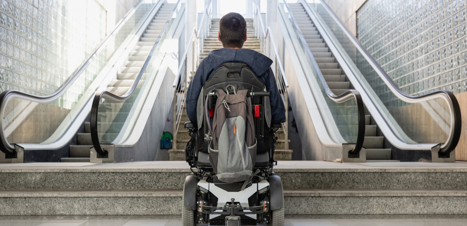 Man in wheelchair at bottom of inaccessible escalators, looking up