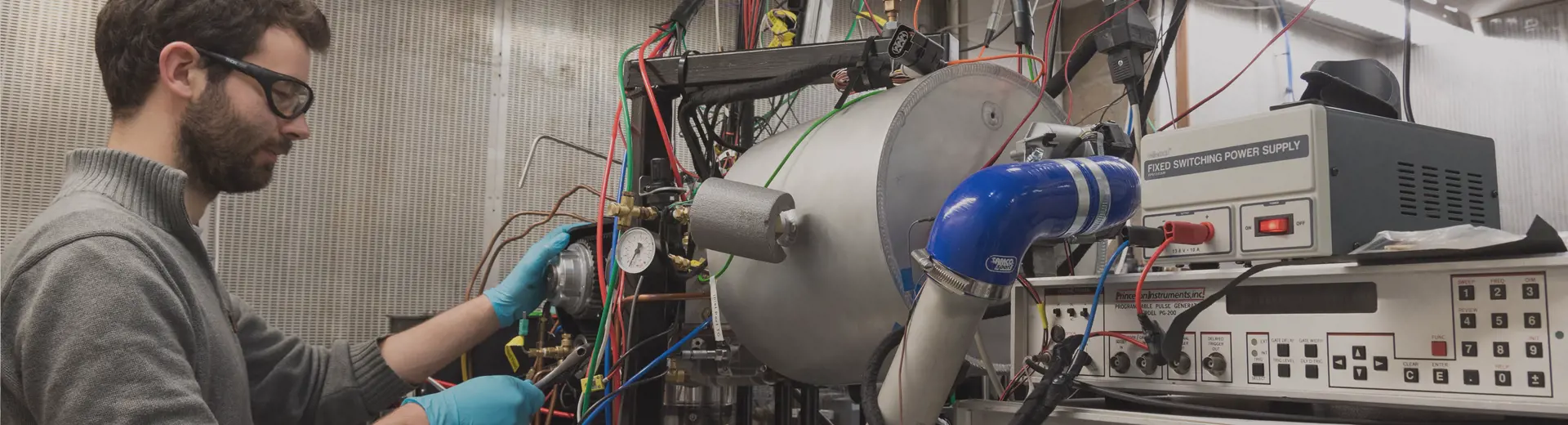 DPhil student wearing lab glasses and gloves working on large machine