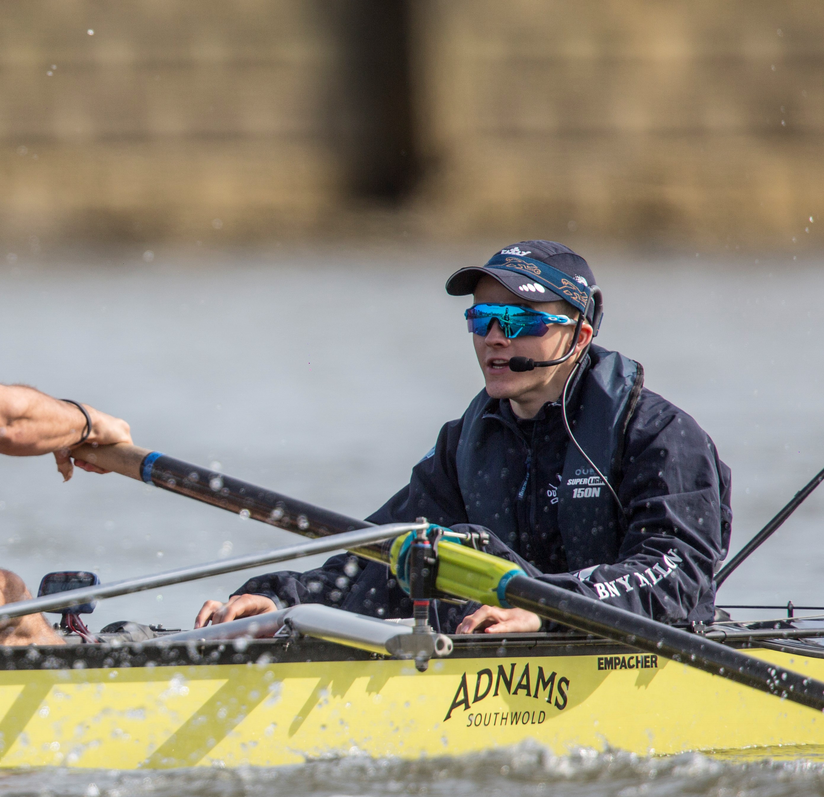 Cox wearing hat and sunglasses in yellow rowing boat in action on the Thames