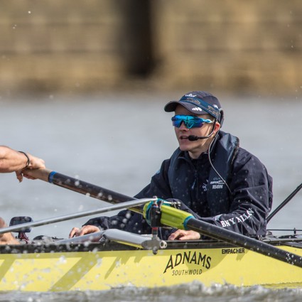 Cox wearing hat and sunglasses in yellow rowing boat in action on the Thames