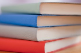 A pile of 4 books in red, grey, blue and light green, with their spines facing the camera