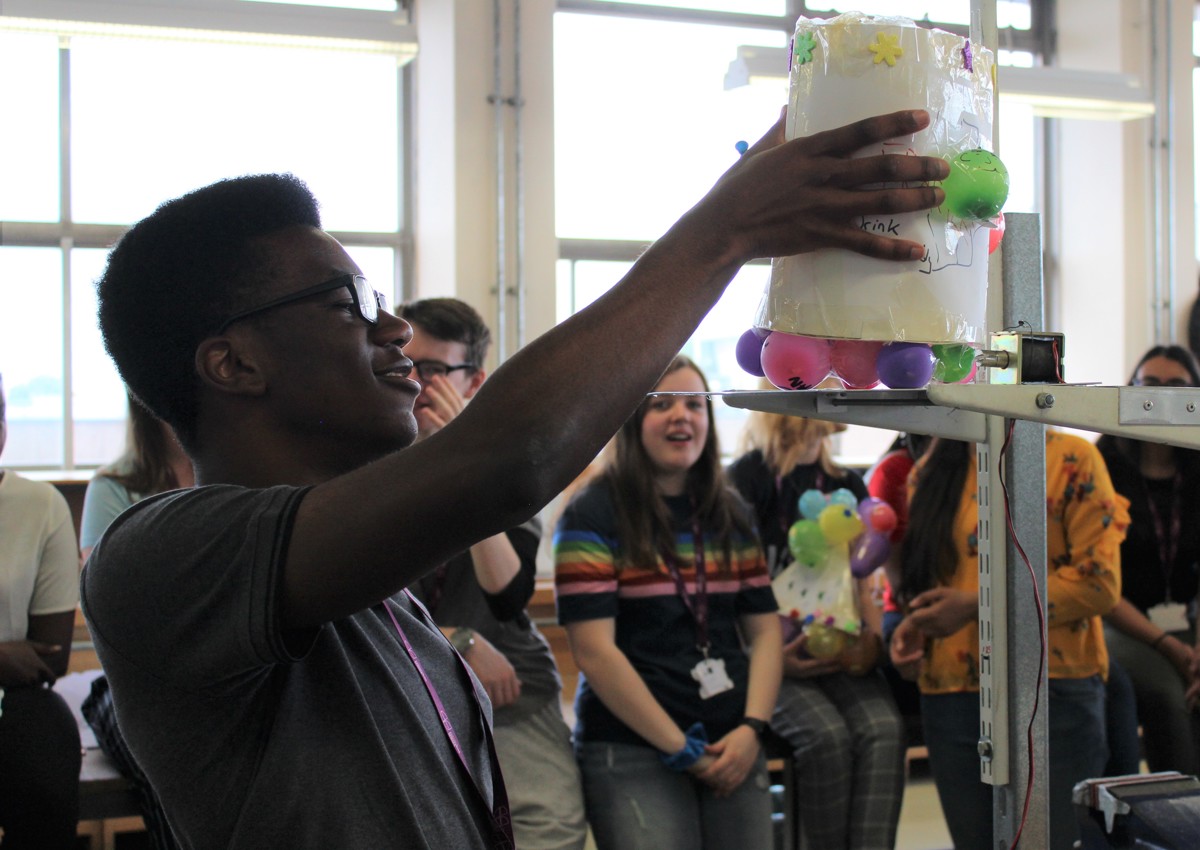 Student placing balloon project on scales infront of classmates