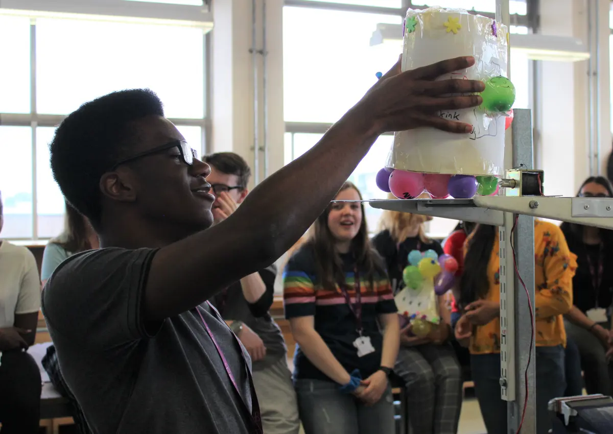 Student placing balloon project on scales infront of classmates