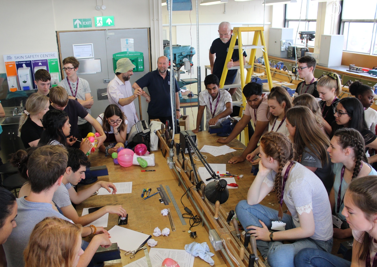 Large group of school students surrounding workshop benches