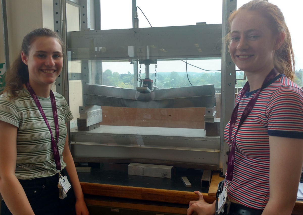 Two female school students standing by machine in the Beam Lab during the Headstart outreach programme