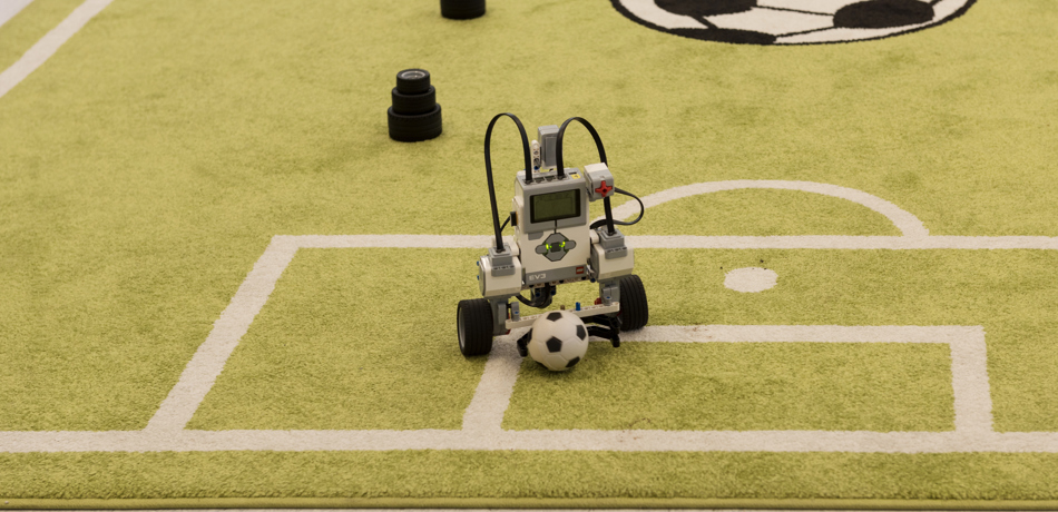 Small robot on miniature football pitch with football