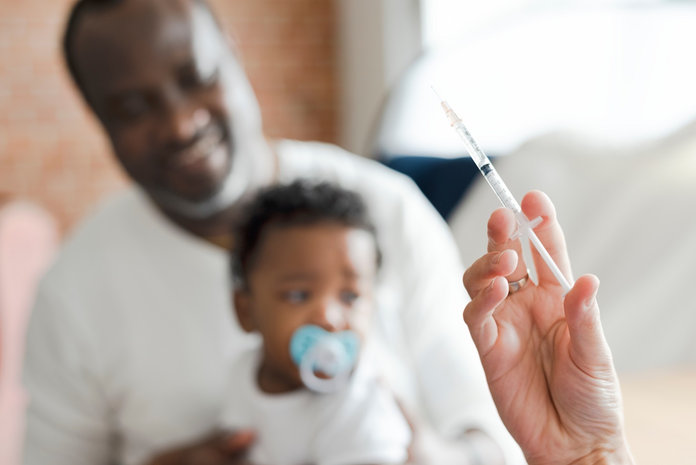 Medical professional prepares to give immunisation to child seated on parent's lap