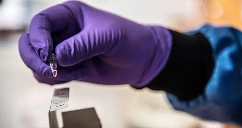 Researcher wearing PPE holding a vial of coronavirus sample