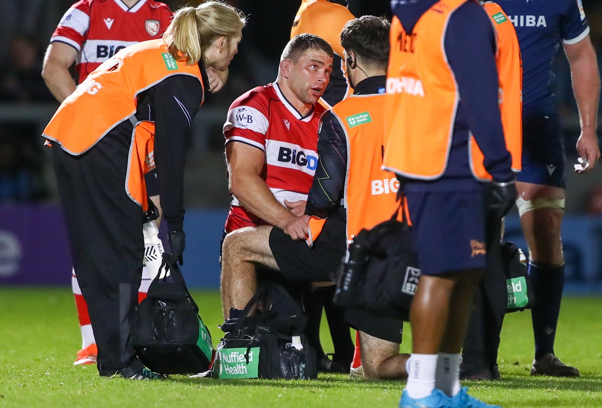 Support staff surround an injured rugby player on a pitch
