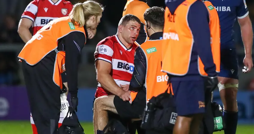 Support staff surround an injured rugby player on a pitch