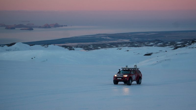 Red vehicle on glacier at sunset in Iceland. 