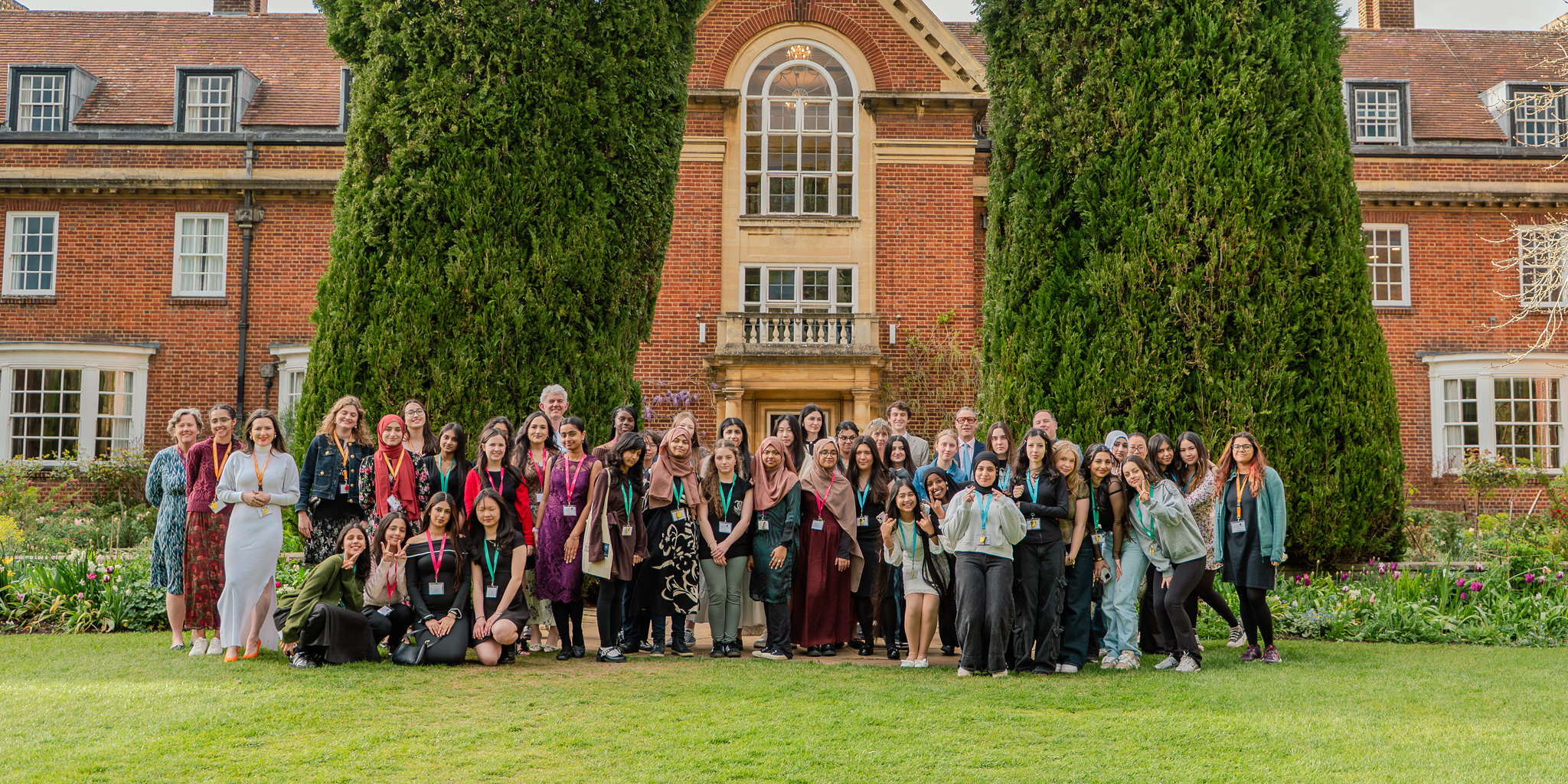A large group of students and staff stand together on a lawn in front of  red-brick St Hugh's college during the Uncover Engineering residential programme.