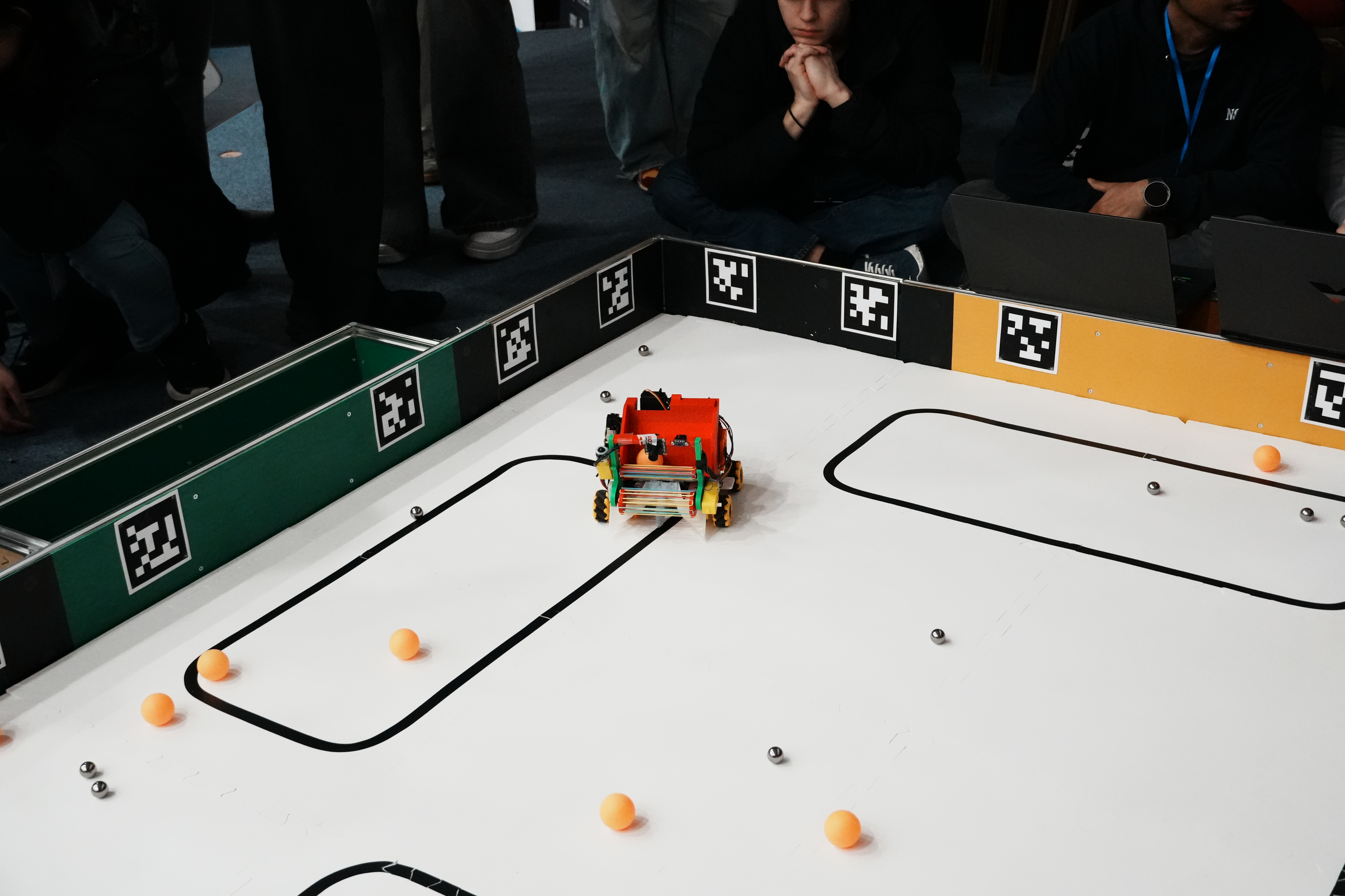 Autonomous robot navigating a competition arena with ping pong balls and metal bearings, surrounded by AprilTag markers.