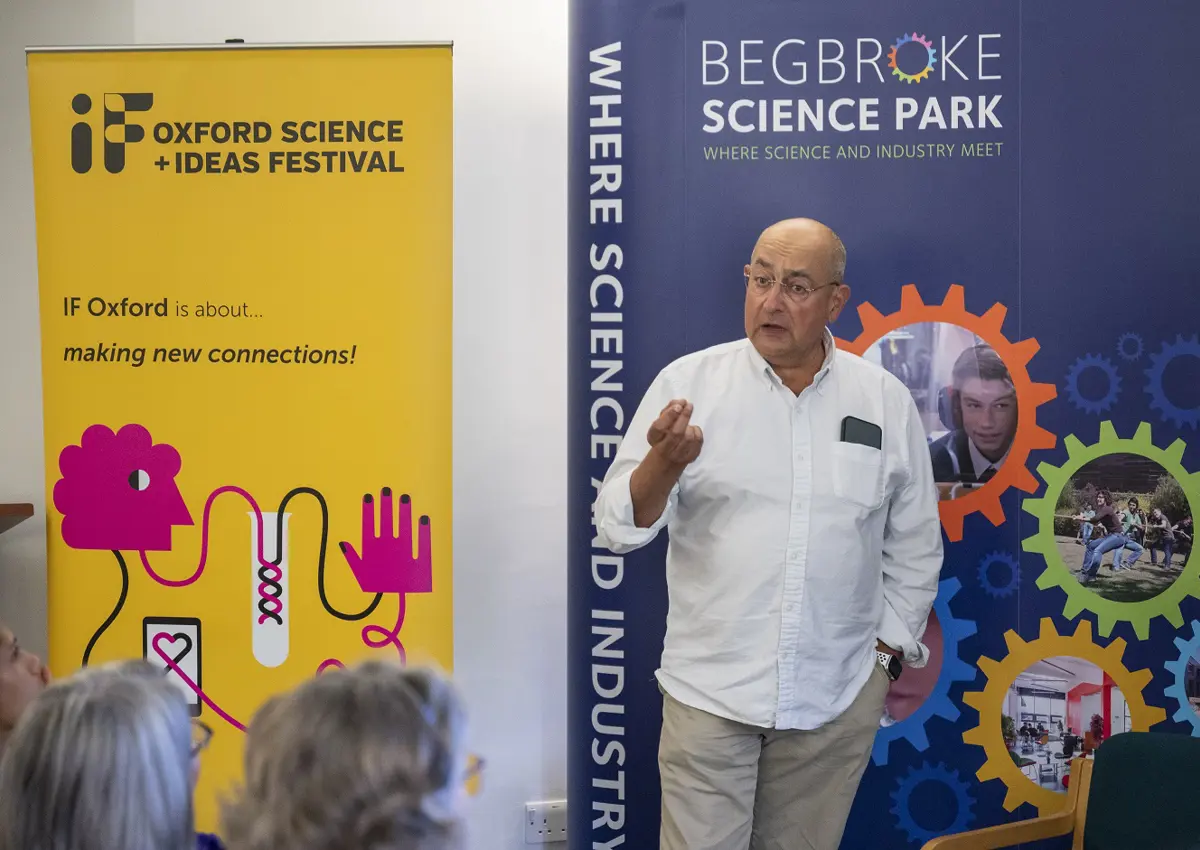 A low resolution image of Professor Ian Thompson stood in front of two roller banners, talking to an audience.