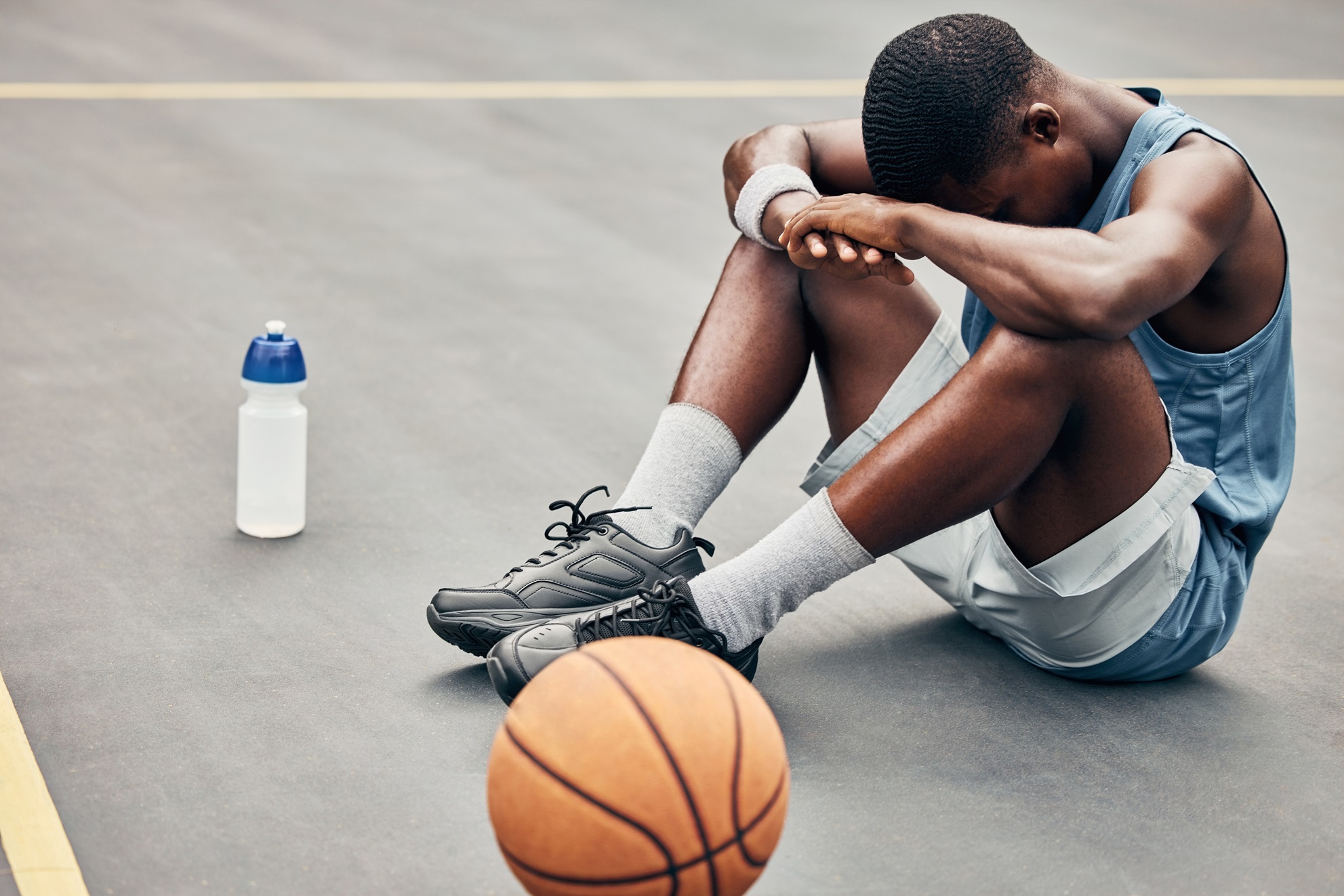 Stock image: Young male basketball player sits on floor after game, resting head on arms