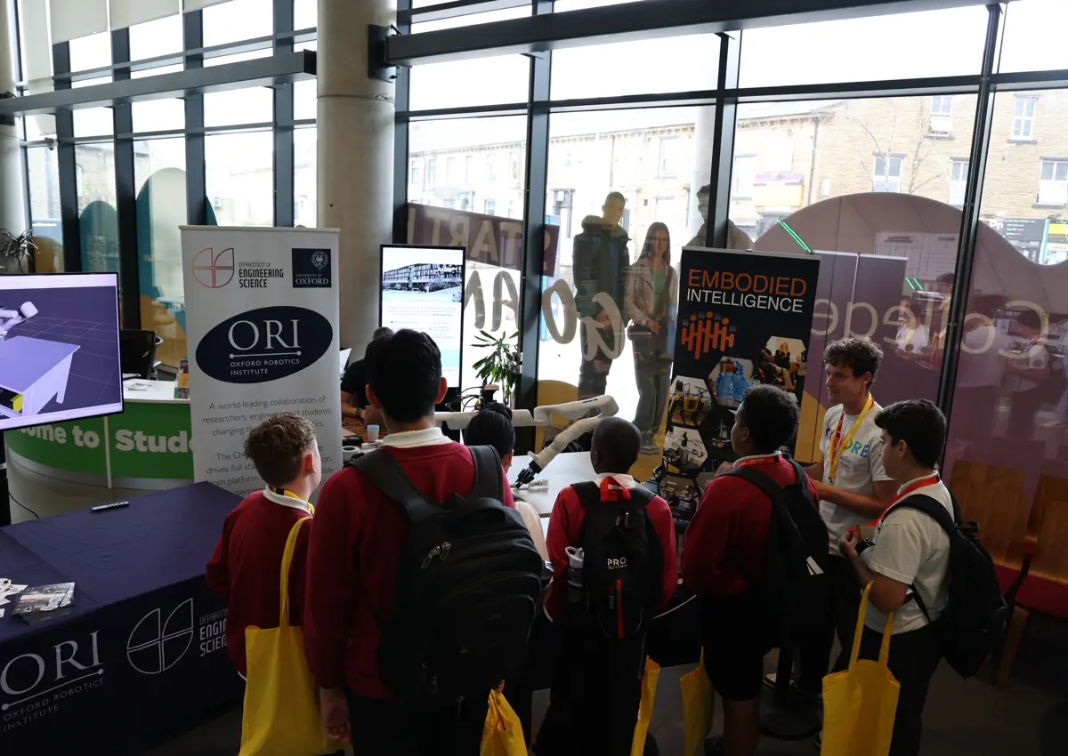 A group of school-aged children stands in front of Frank the robot, watching a hands-on demonstration by Oxford researchers during the Oxplore Festival. The robot’s arms are mid-motion.