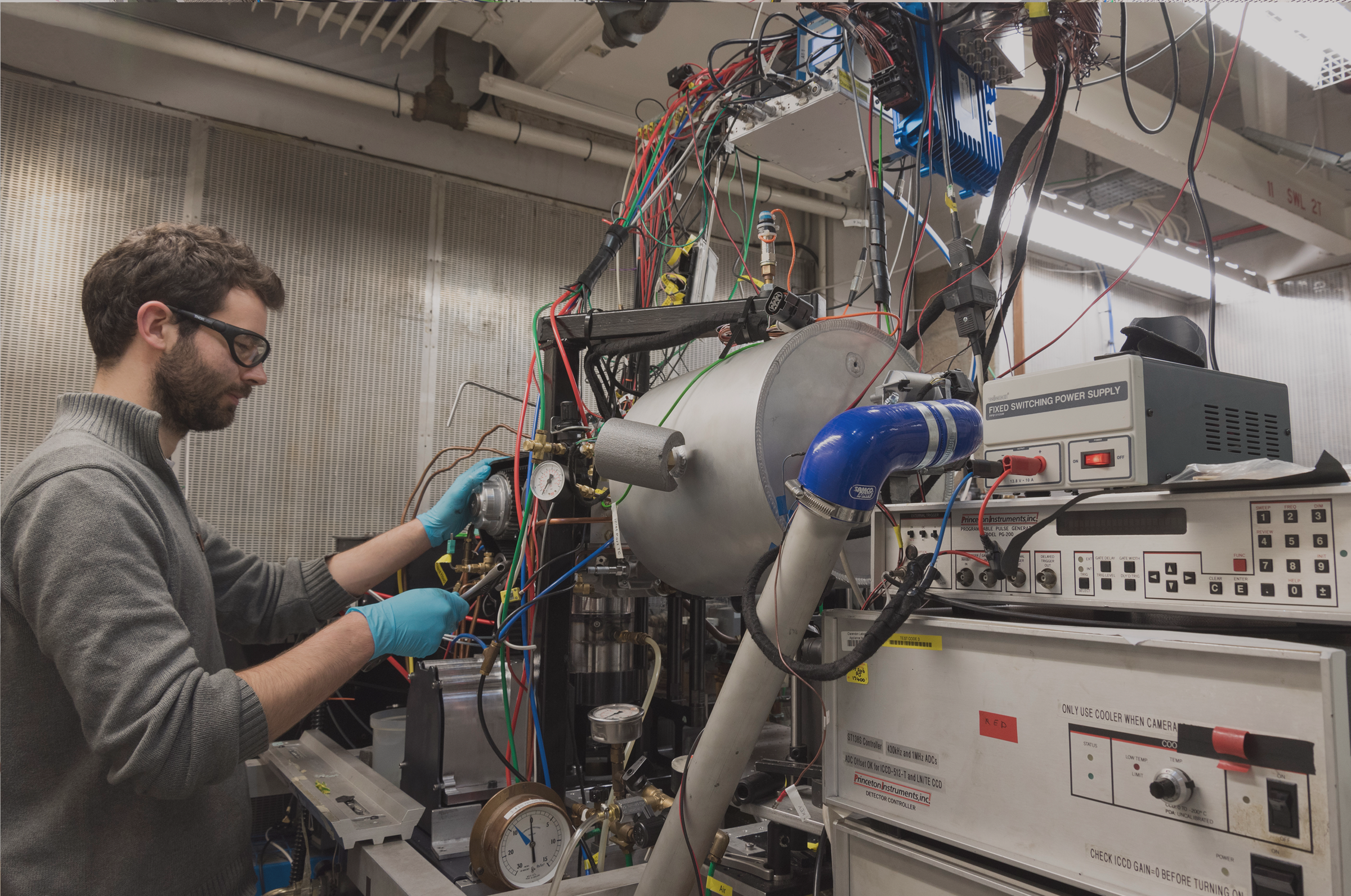 DPhil student wearing lab glasses and gloves working on large machine