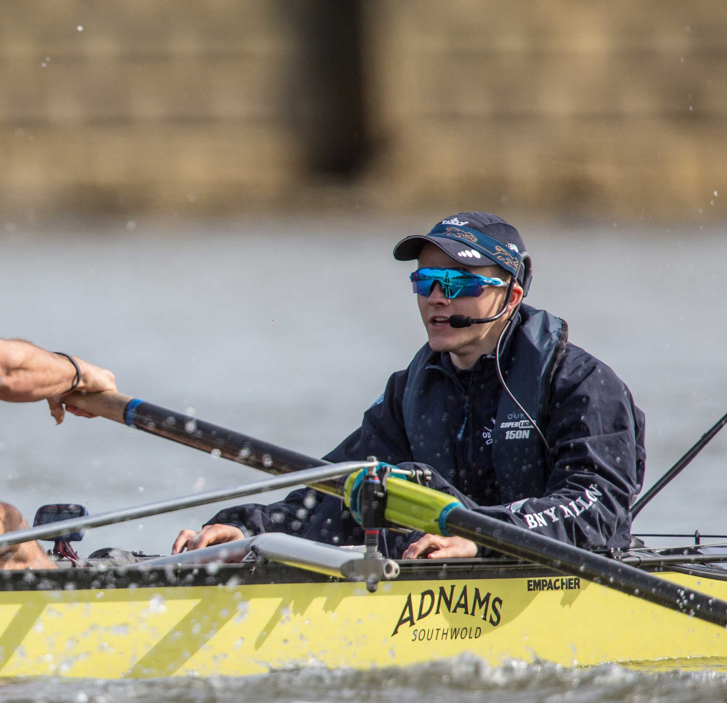 Cox wearing hat and sunglasses in yellow rowing boat in action on the Thames