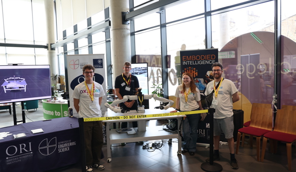 Four Oxford Robotics Institute team members pose with Frank the robot at the Oxplore Festival stand. Banners and educational materials promoting robotics research are visible behind them.