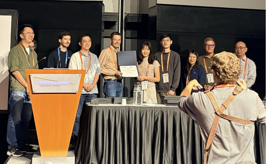 The photo shows some of the authors at the conference award ceremony. Chuhan Zhang is receiving the award with Junyu Xie standing to her left.