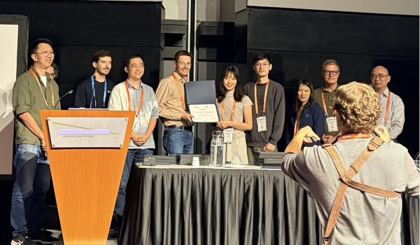 The photo shows some of the authors at the conference award ceremony. Chuhan Zhang is receiving the award with Junyu Xie standing to her left.