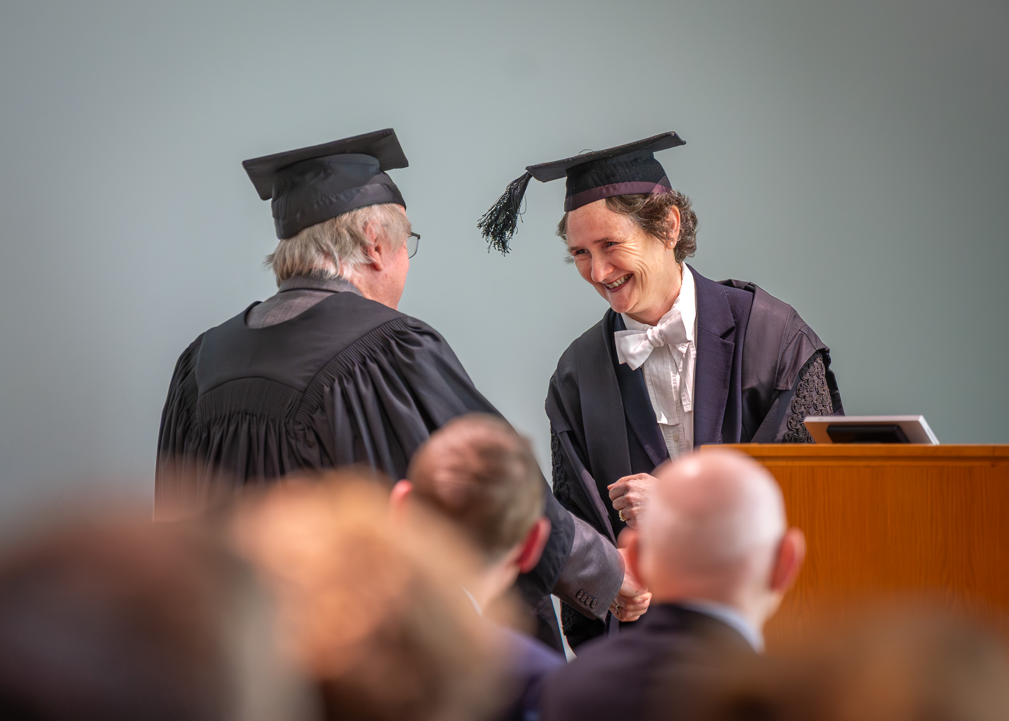 Vice-Chancellor Irene Tracey smiles as she shakes hands with Professor Stan Whittingham, both wearing academic dress, during the inaugural John Goodenough Lecture.