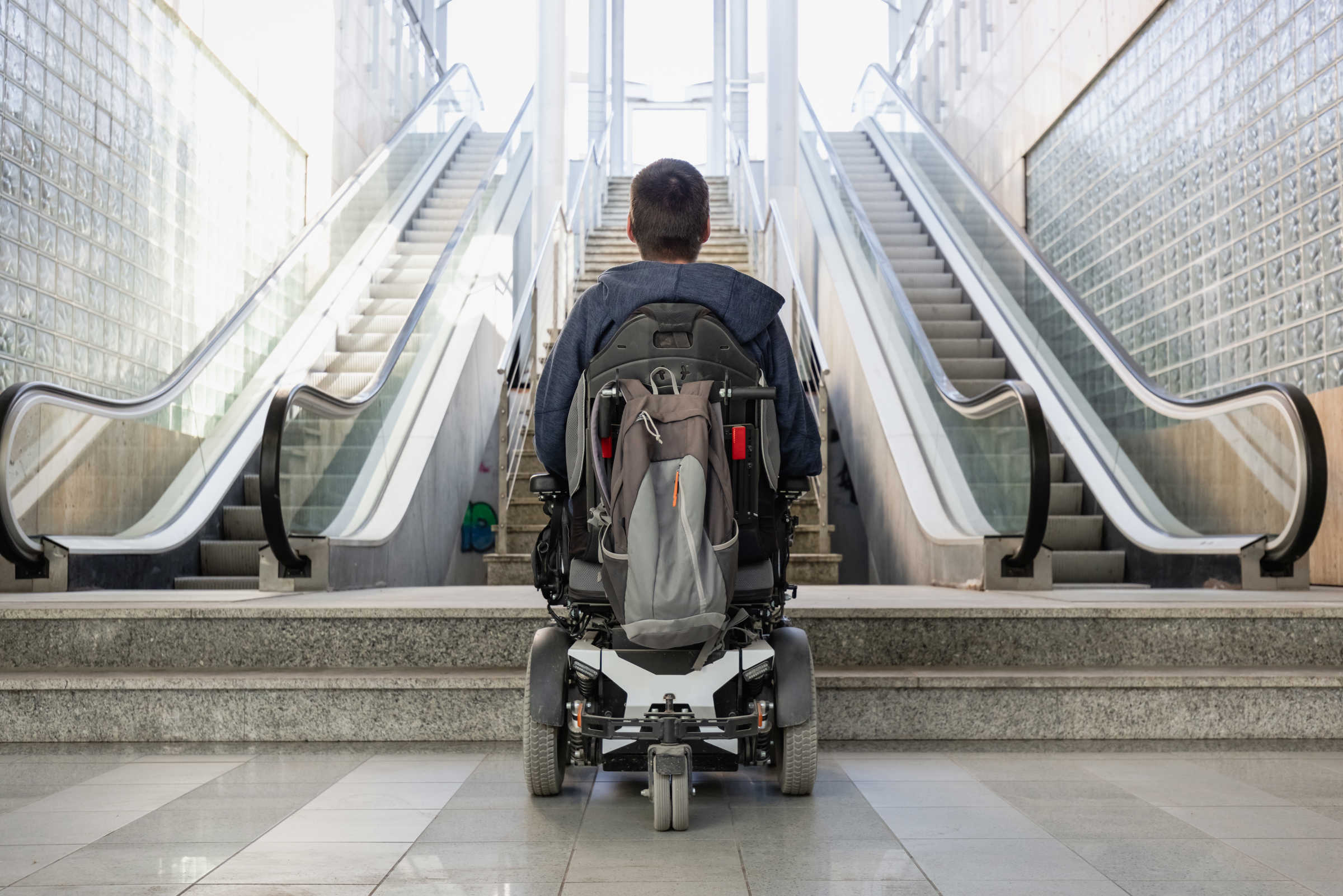 Man in wheelchair at bottom of inaccessible escalators, looking up