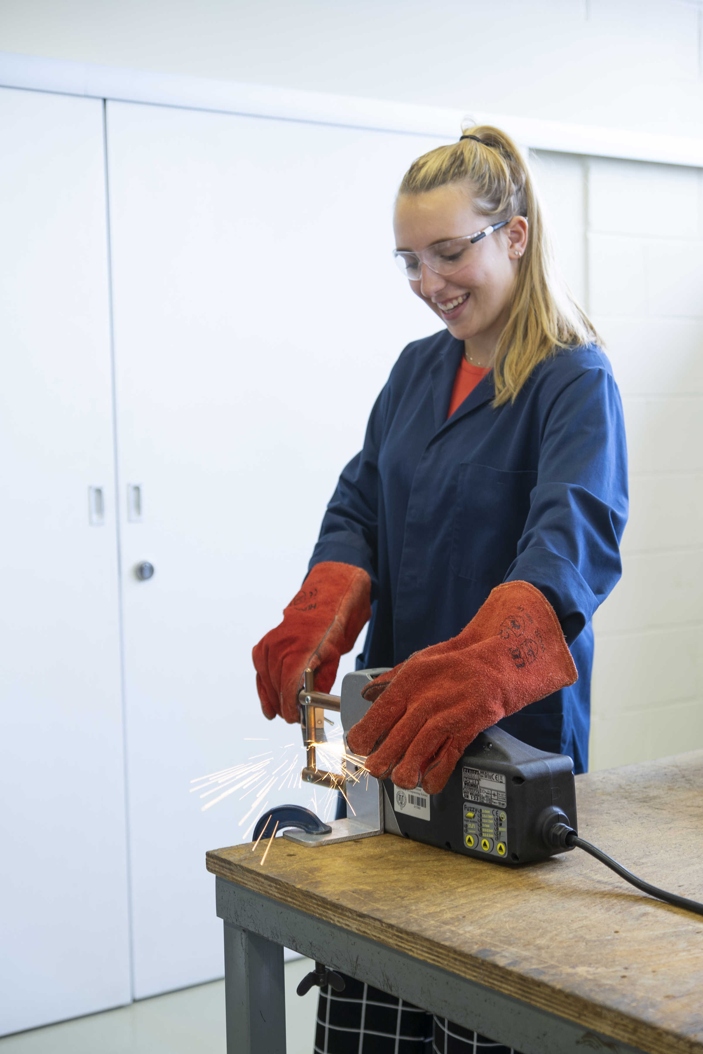 Student in full safety gear using machine with sparks