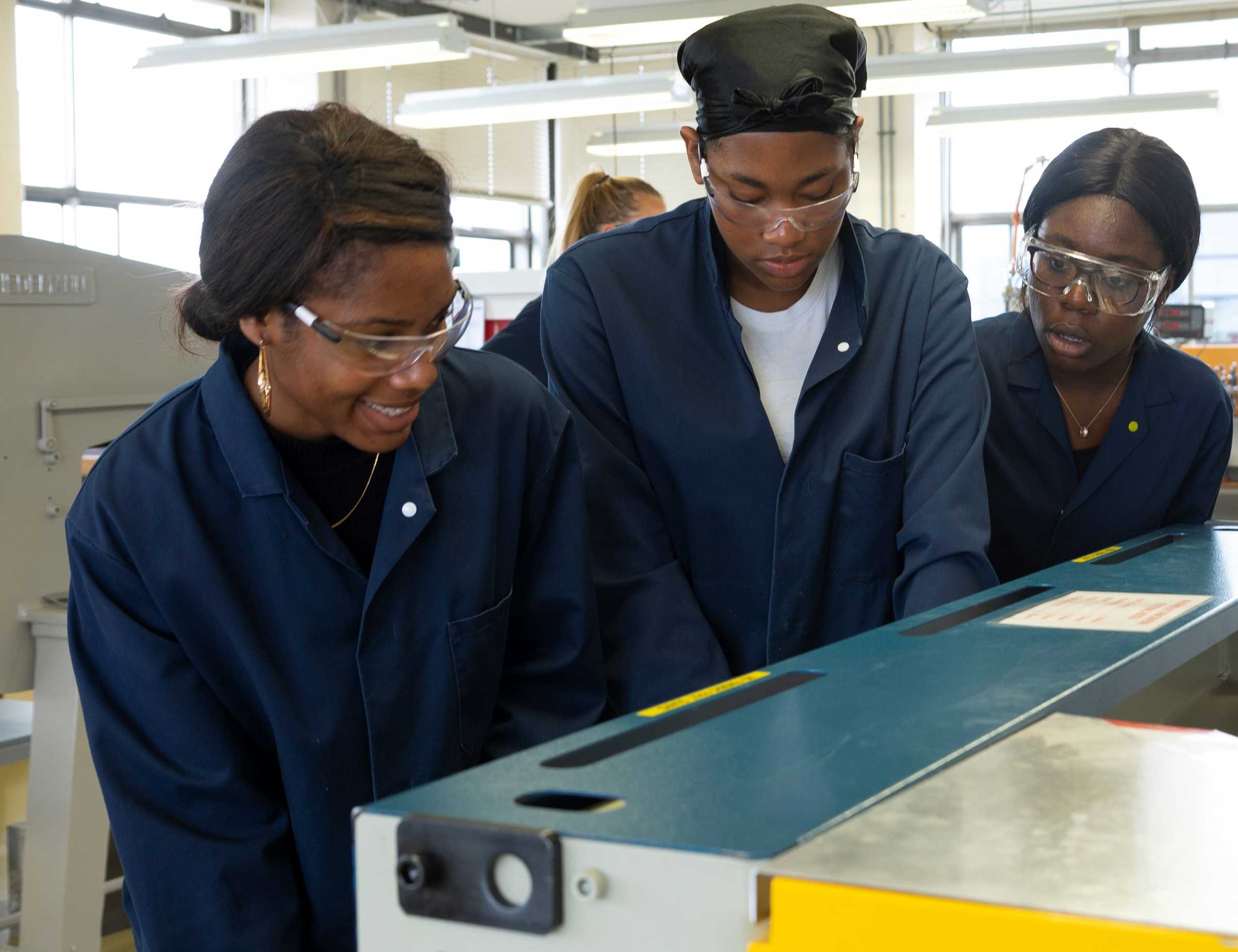 Three students in lab coats looking at a machine