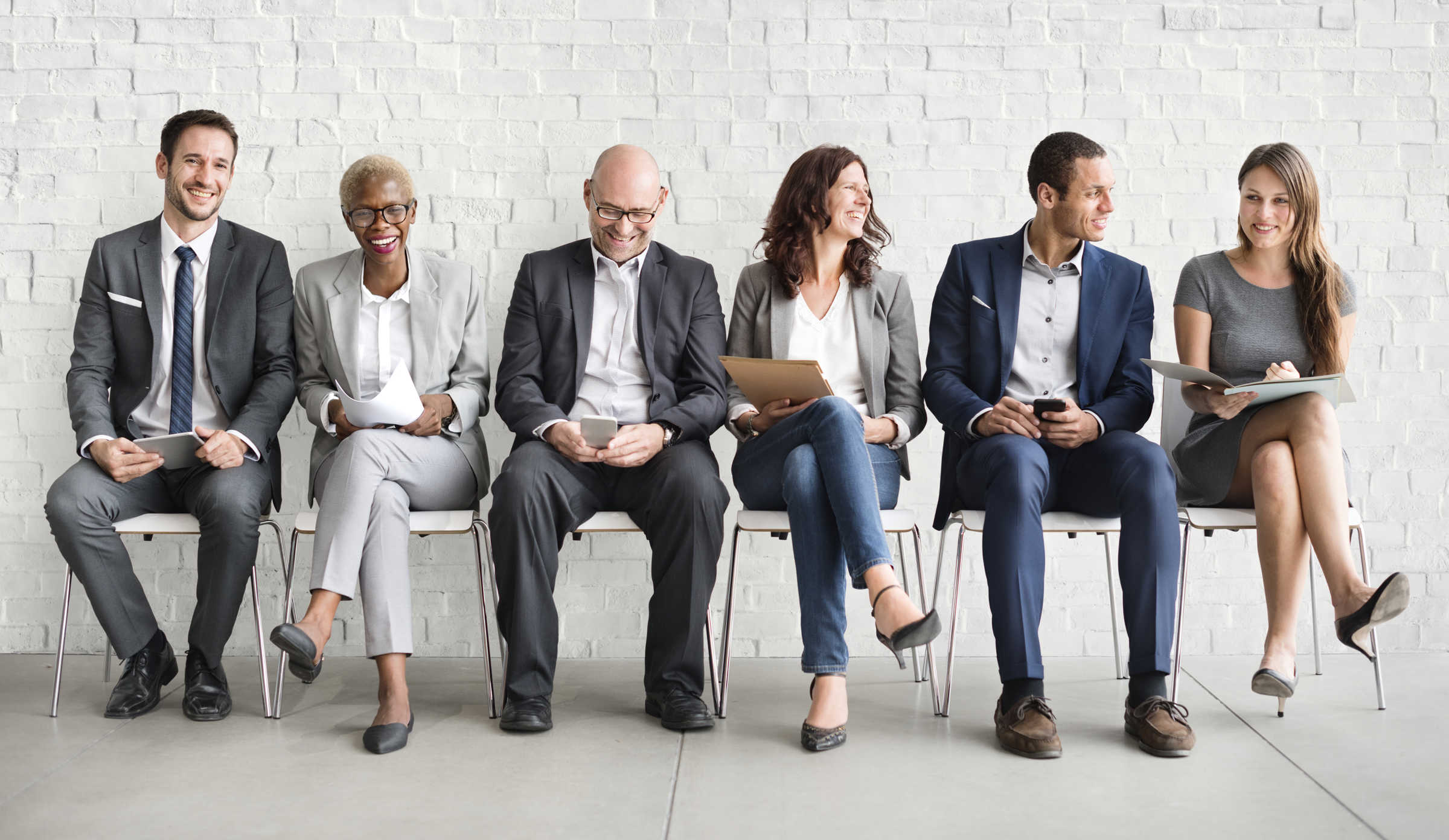 Row of people sat in chairs laughing and wearing smart business clothes