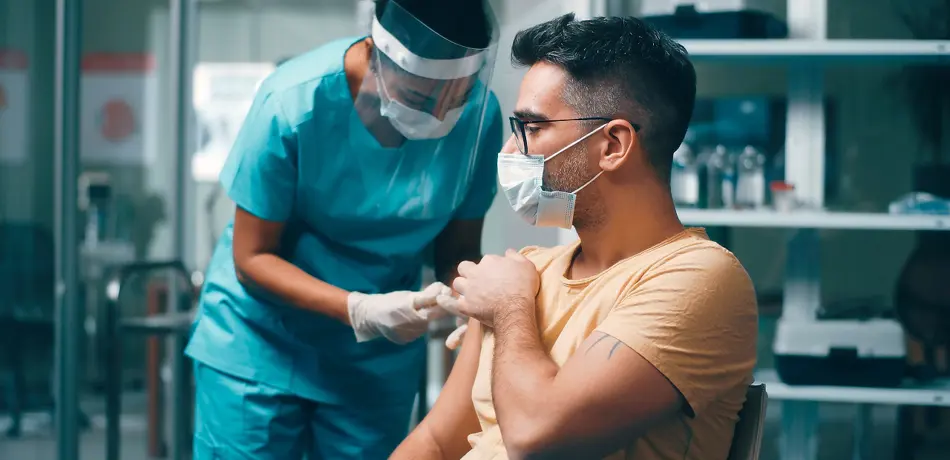 Stock image - medical professional giving a man in a face mask an injection in his right arm
