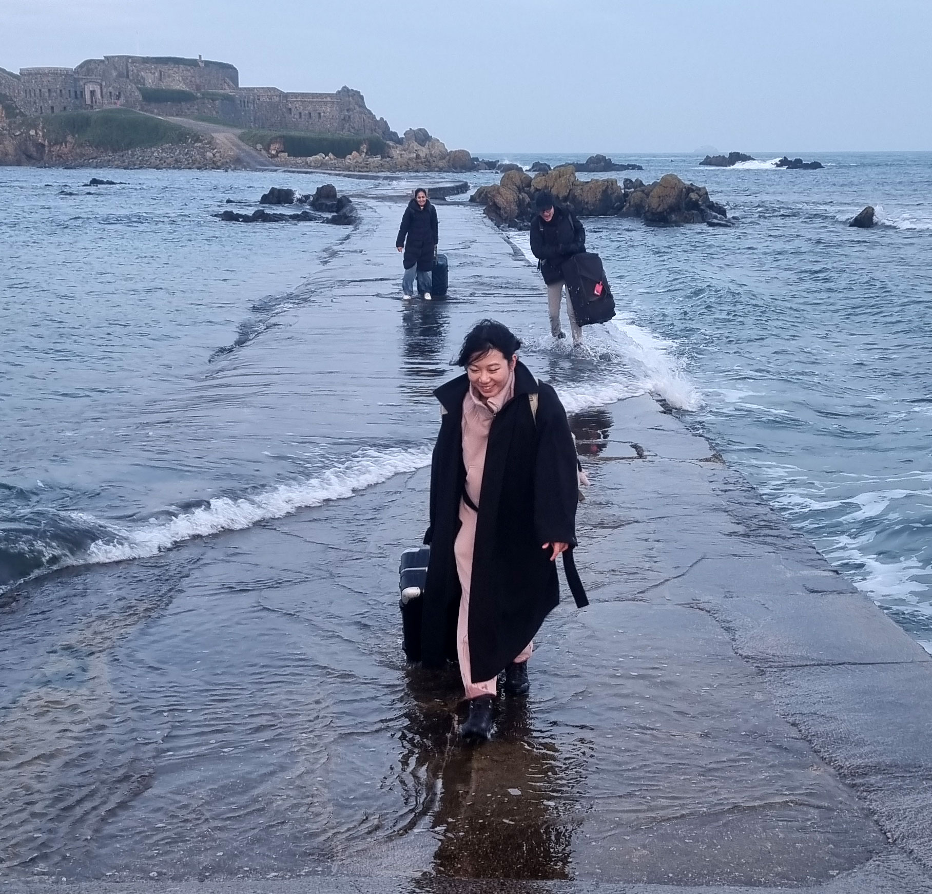 Researchers walking along the fort’s causeway with luggage as seawater flows across the path.