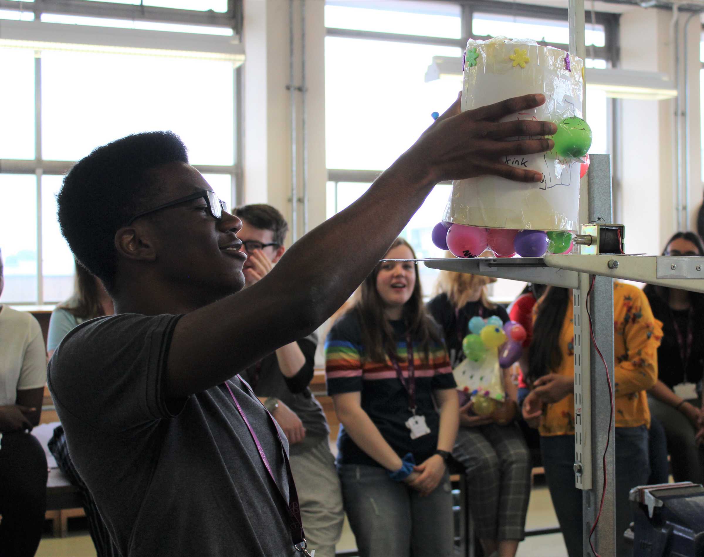 Student placing balloon project on scales infront of classmates