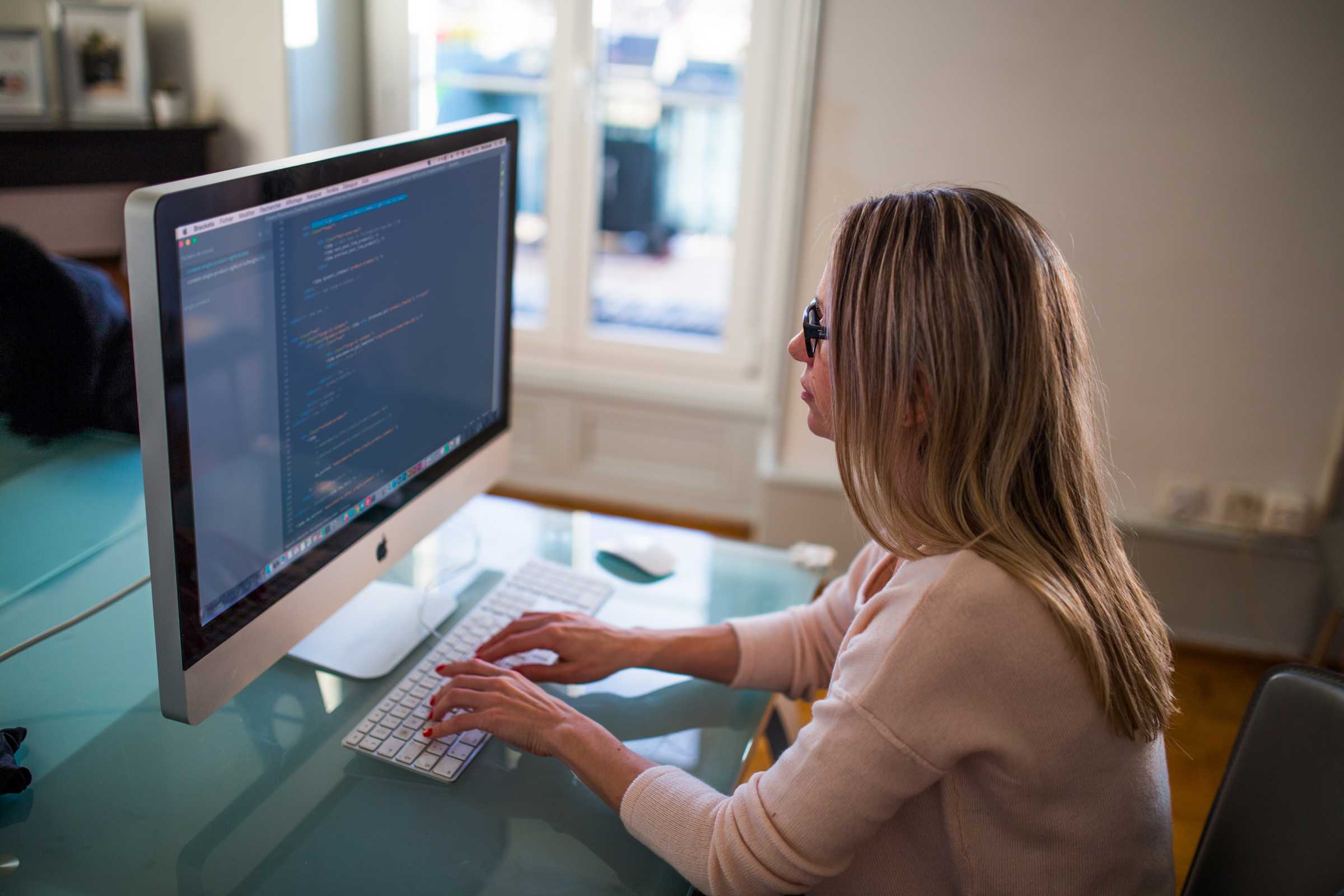 Blonde woman working at a white computer 