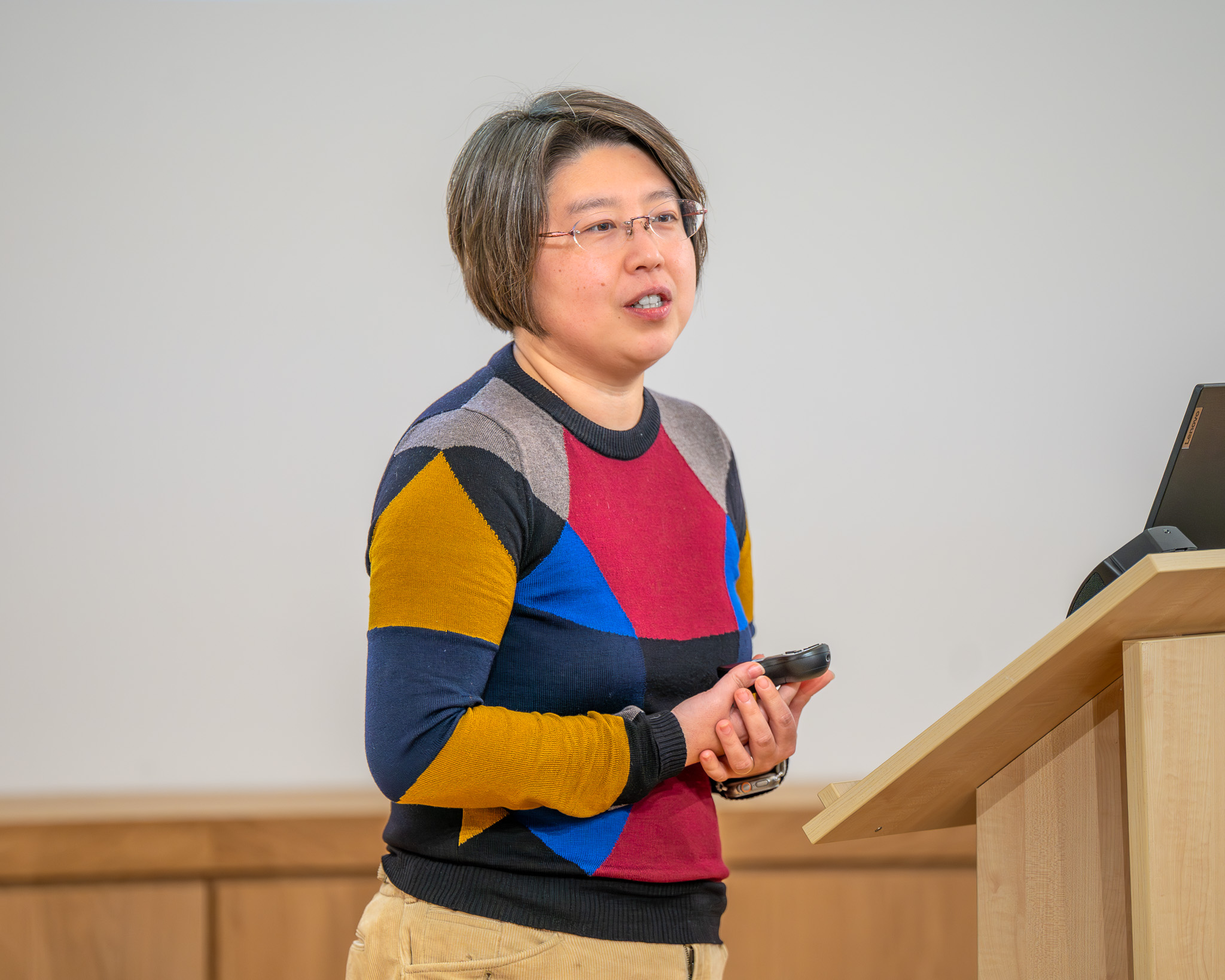 Dr Yvonne (Huiqi) Lu stands at a lectern holding a presentation remote while addressing the audience, with a laptop beside her. She is delivering her talk as part of the OxBridge Women in Engineering event.