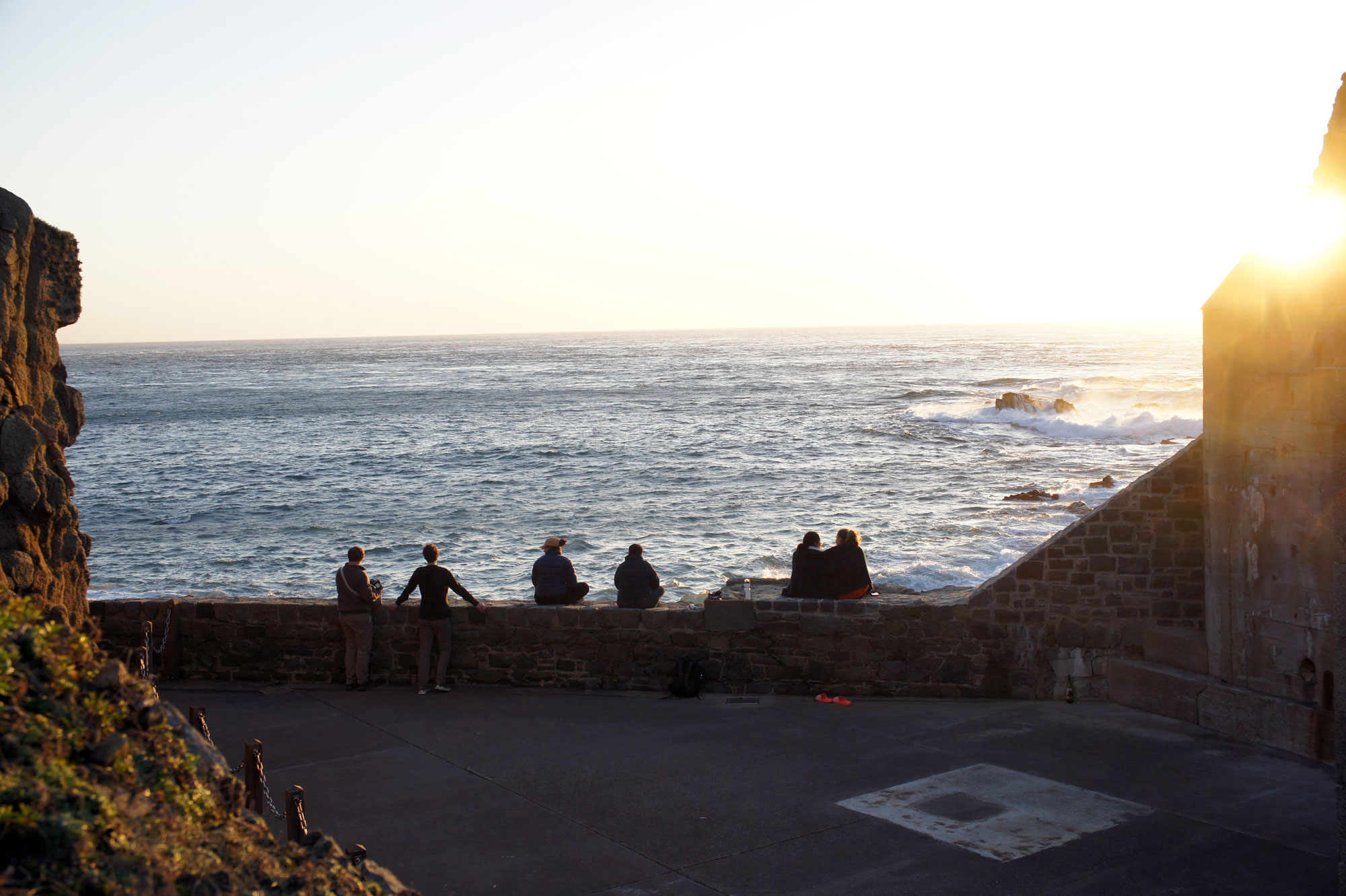 Members of the group sitting on the stone walls of Fort Clonque, overlooking the sea and rugged cliffs below.