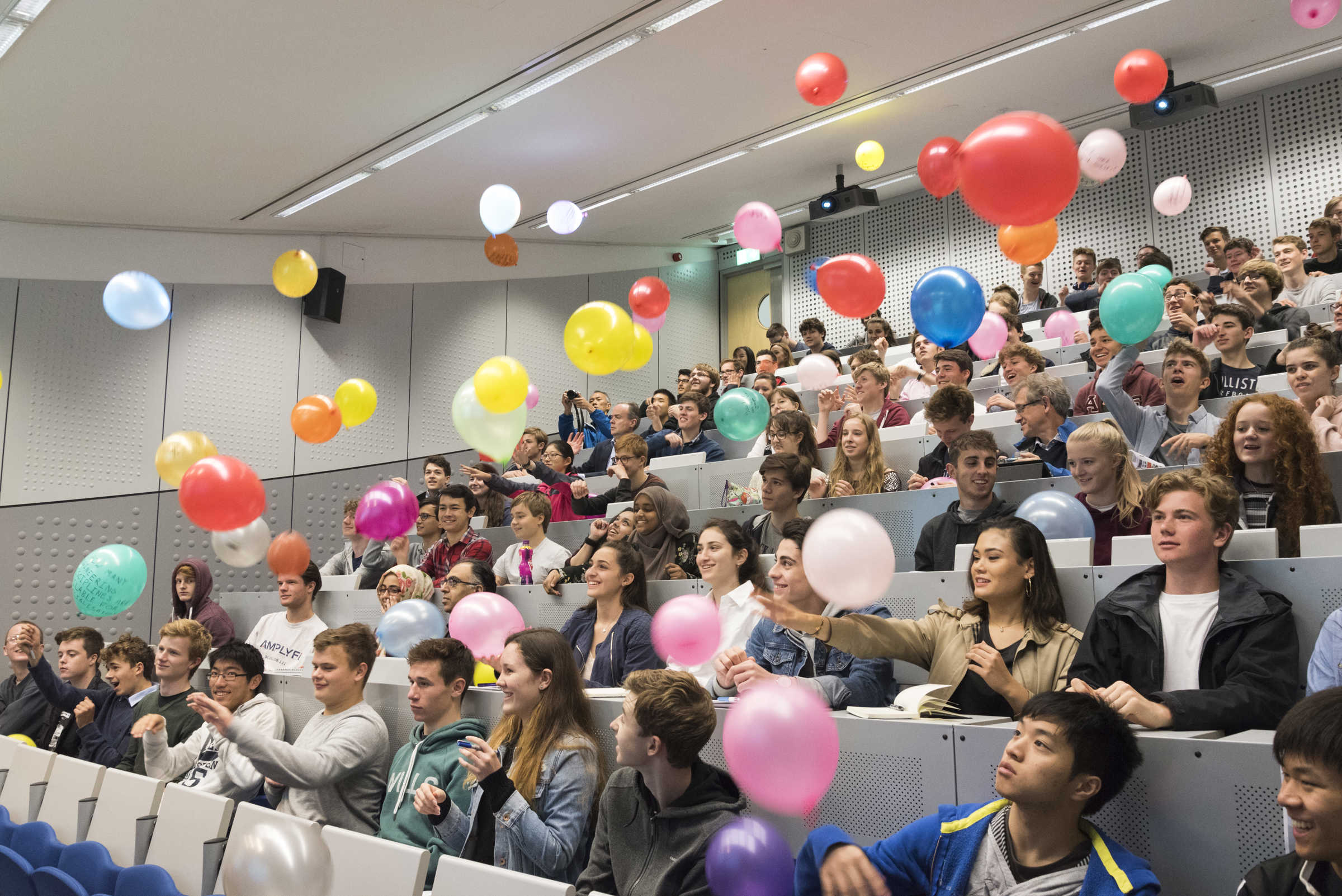 Lecture theatre of people throwing balloons into the air, at open day 2017