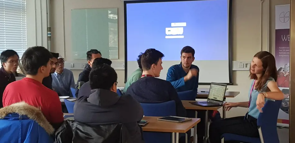 Students in classroom sat with teachers, discussing.